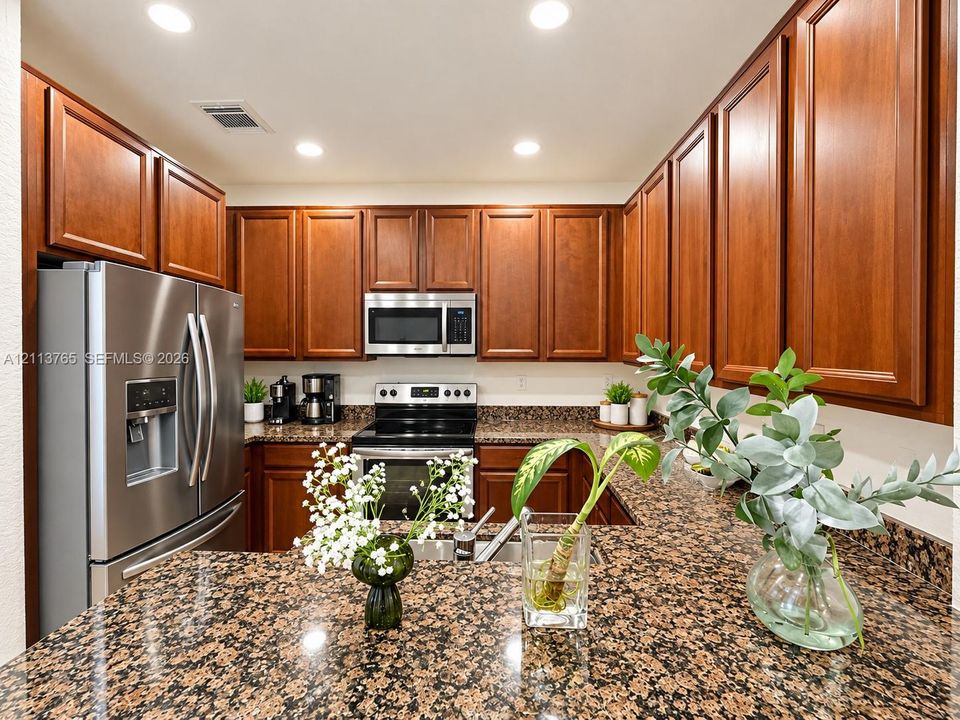 Kitchen featuring rich wood-finish cabinetry, stone countertops, and stainless steel appliances including a built-in microwave, range, and refrigerator