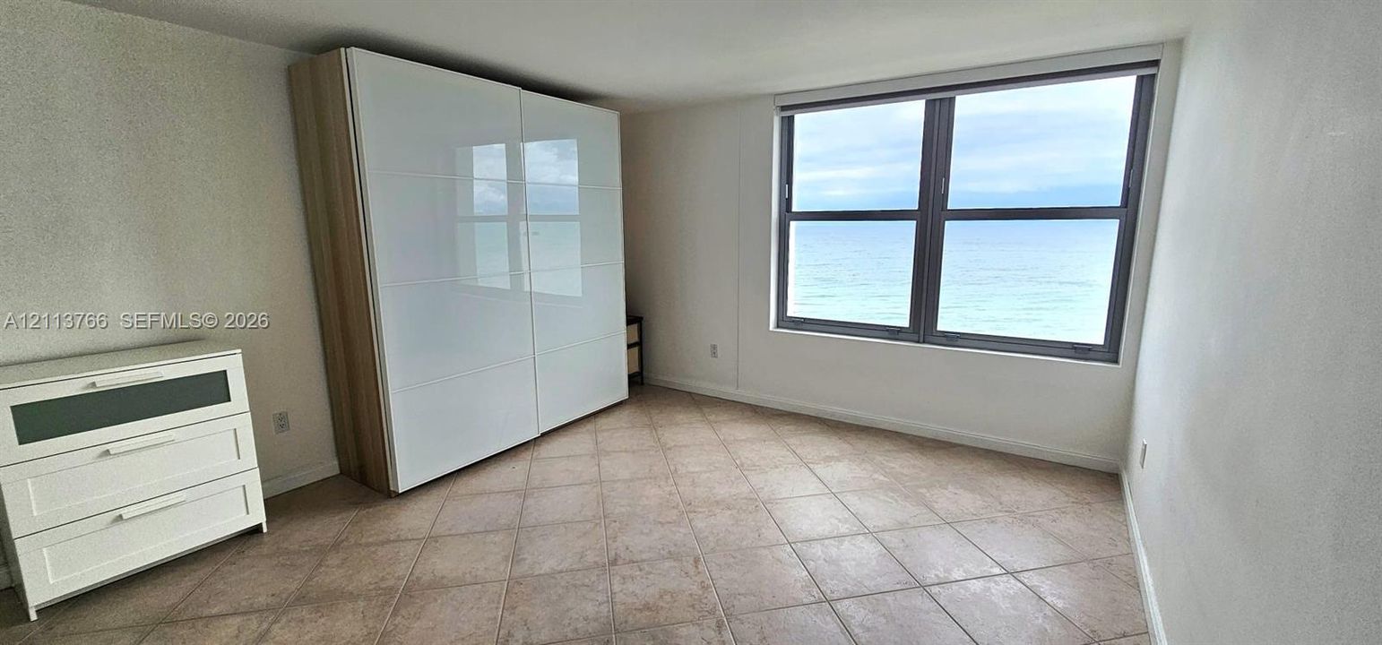 Open-concept interior featuring large-format tile flooring, mirrored wall accents, built-in entertainment cabinetry, and expansive windows