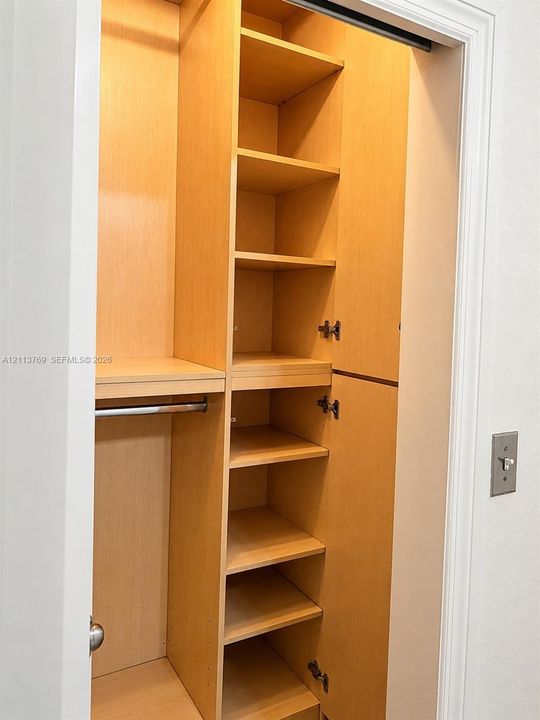 Custom closet storage featuring light wood-finish shelving, an integrated hanging rod, and enclosed cabinetry