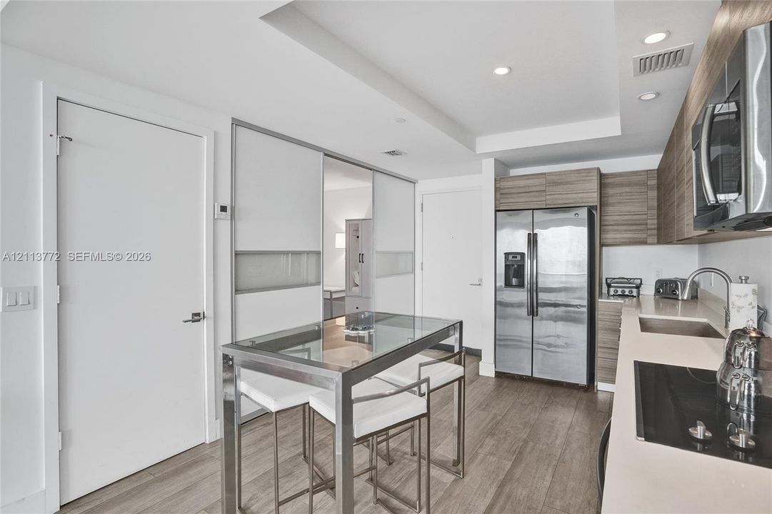 Kitchen featuring horizontal wood-grain cabinetry, stainless steel side-by-side refrigerator, recessed lighting, wood-finish flooring, and solid-surface countertops