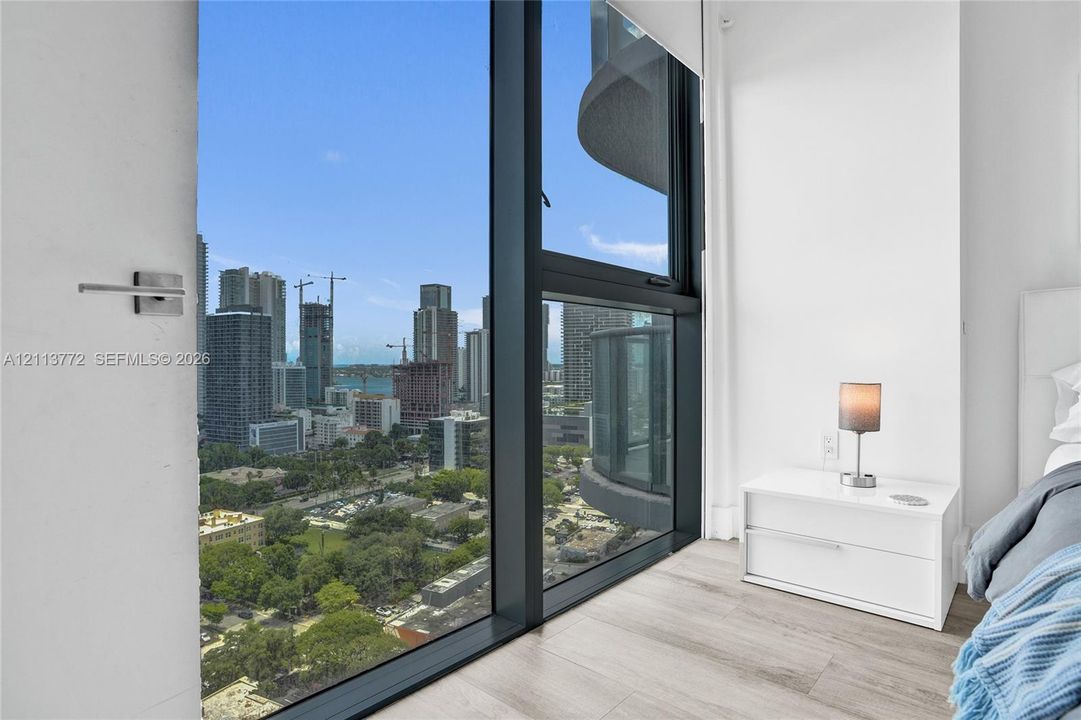 Floor-to-ceiling windows featuring dark metal framing, wood-finish flooring, and expansive urban scenery