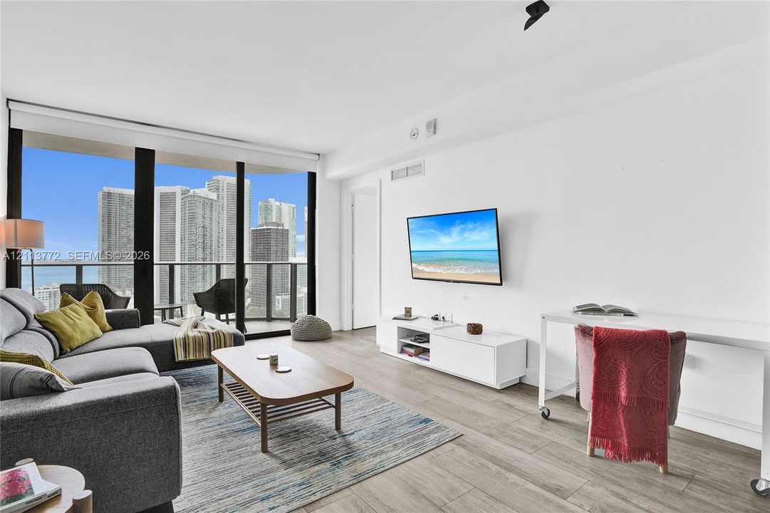 Floor-to-ceiling windows, wood-finish flooring, and a private balcony featuring a glass and metal railing