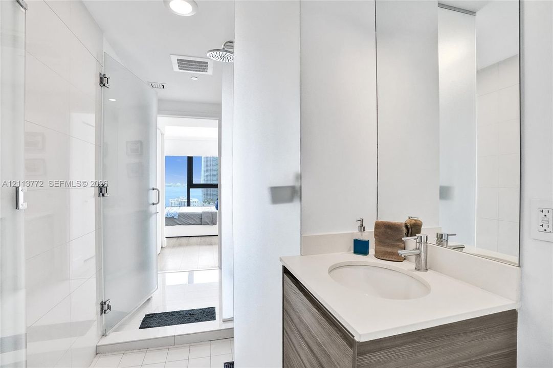 Bathroom featuring a wood-finish vanity with a light-toned countertop, integrated sink, chrome faucet, glass-enclosed shower, and full-height wall mirror