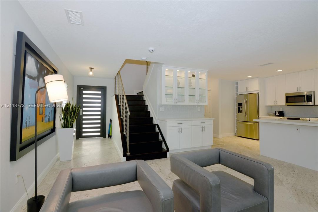 Modern entryway featuring a multi-paneled glass front door, stone-finish flooring, and a staircase with dark treads and metal railings