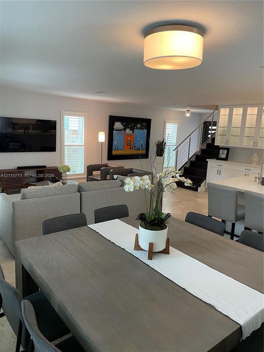 Open concept interior featuring stone tile flooring, built-in glass-front cabinetry, a contemporary drum-style ceiling light, and a staircase with metal horizontal balusters