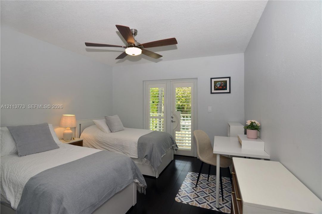 Dark-toned flooring, ceiling-mounted fan with integrated lighting, and glass-paned double doors with slatted shutters