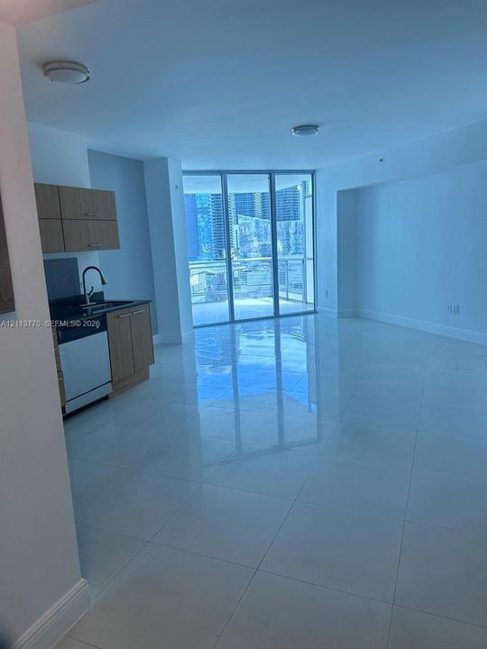 Polished stone tile flooring, floor-to-ceiling glass sliding doors, cabinetry with wood-finish doors, dark stone-surface countertops, and stainless steel dishwasher