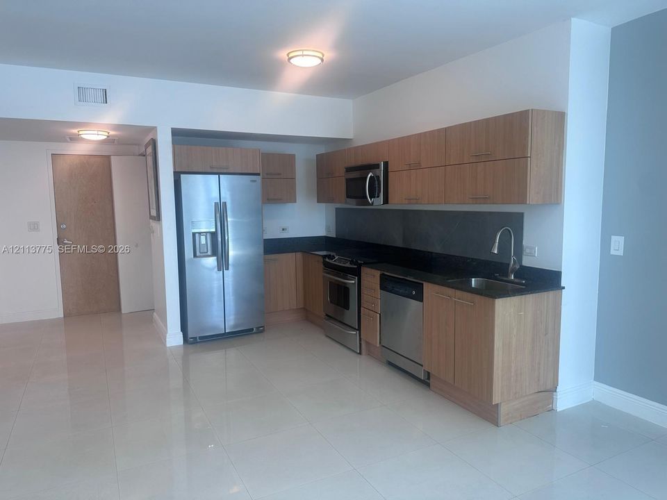 Kitchen featuring flat-panel wood-finish cabinetry, stainless steel appliances, dark stone-finish countertops, tile flooring, and a single-basin undermount sink with a gooseneck faucet