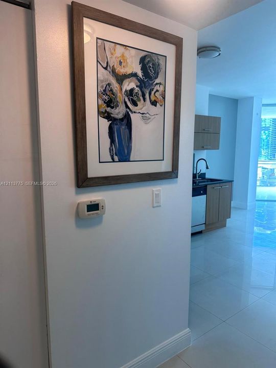Kitchen area featuring light-toned cabinetry, stainless steel dishwasher, dark countertop, and high-gloss tile flooring