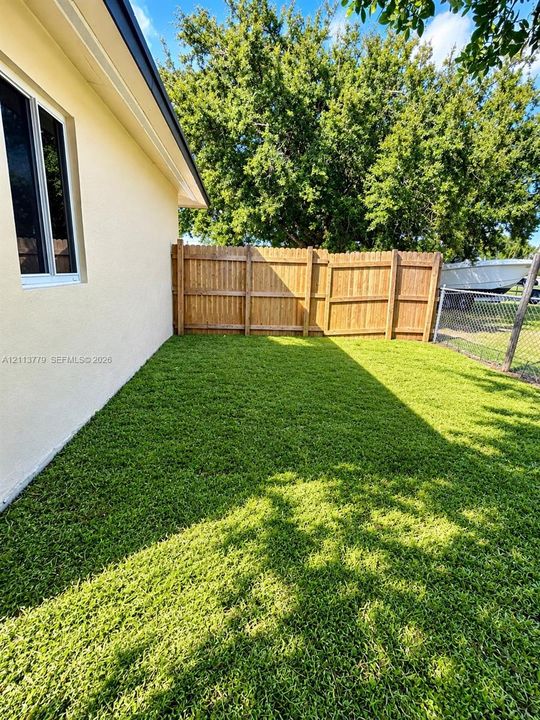 Rear exterior featuring a manicured lawn, wood privacy fencing, and mature trees