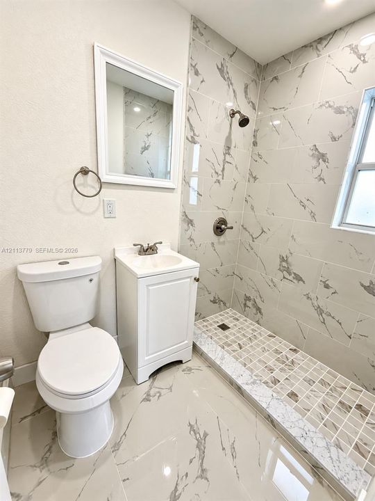 Bathroom featuring large-format tile flooring, a shower with floor-to-ceiling veined tile surrounds, a glass-tile mosaic shower floor, a white vanity with a rectangular sink, and a wall-mounted mirror