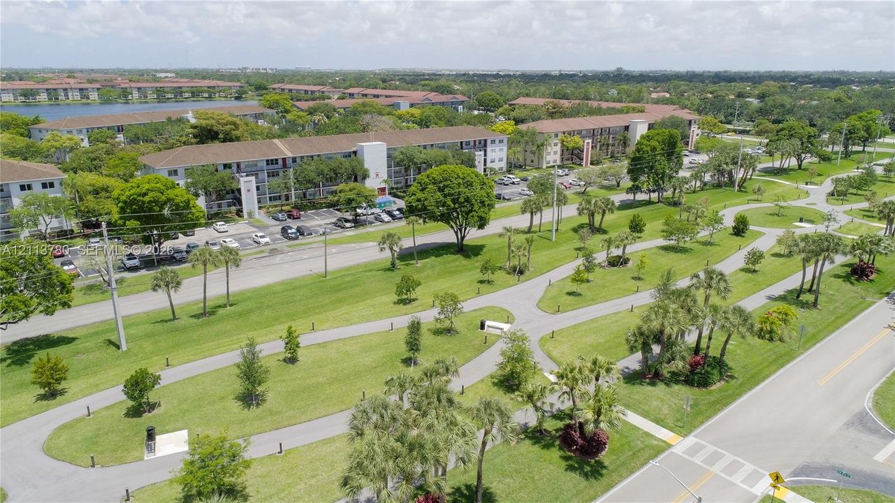 Aerial perspective featuring multi-story residential buildings, paved pedestrian pathways, manicured green space, and mature trees