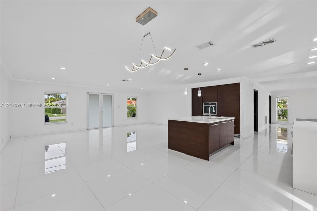 Open-concept interior featuring large-format tile flooring, a center island with a stone countertop, dark wood-finish cabinetry, recessed lighting, and a modern sculptural chandelier
