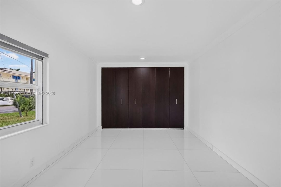 Interior space featuring large-format white tile flooring, recessed ceiling lighting, and floor-to-ceiling built-in cabinetry with dark wood-finish paneling