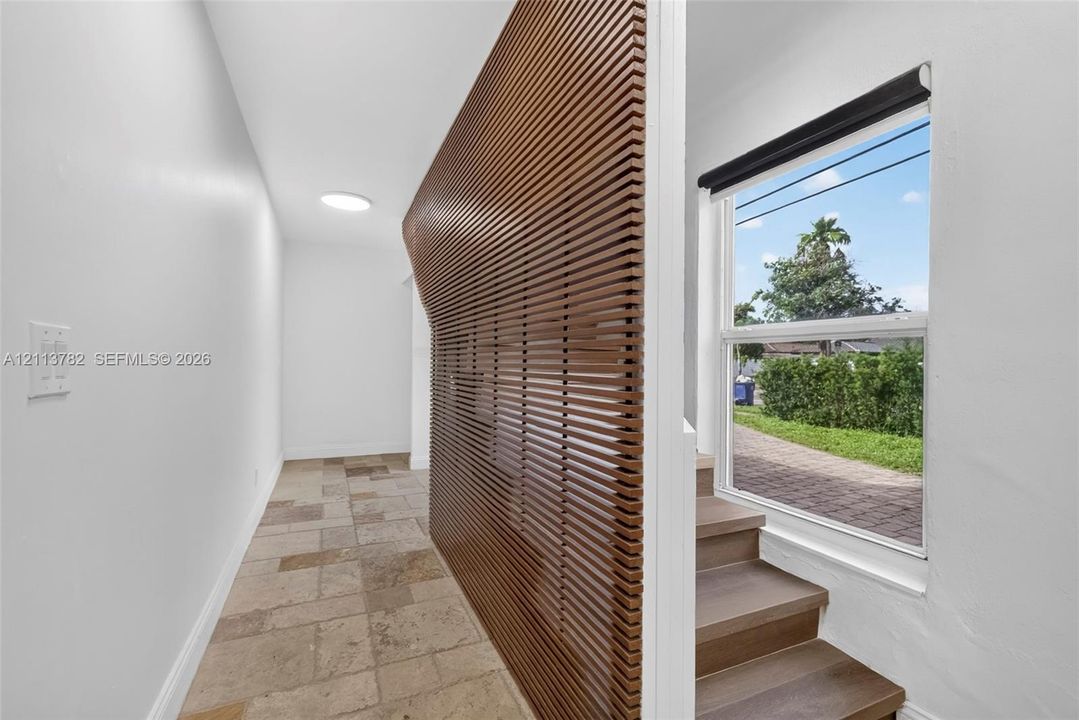 Interior featuring a curved slat-wood wall partition, large-format stone tile flooring, and stairs with wood-finish treads beneath a single-hung window
