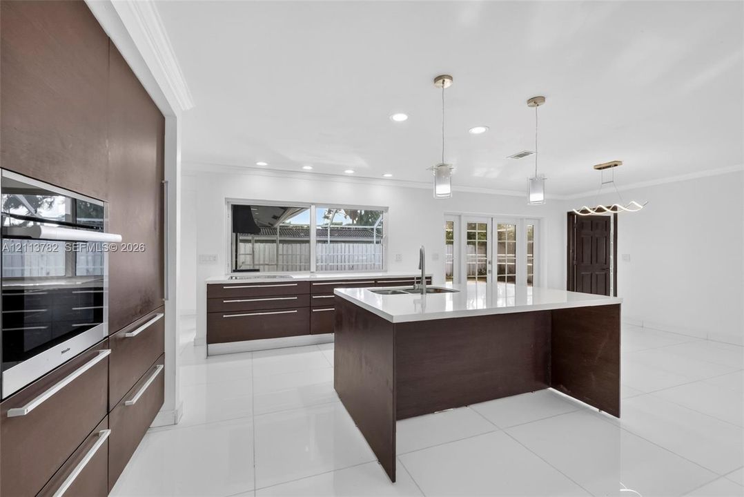 Kitchen featuring flat-panel cabinetry, a central island with a solid-surface countertop, recessed ceiling lighting, pendant light fixtures, and polished tile flooring