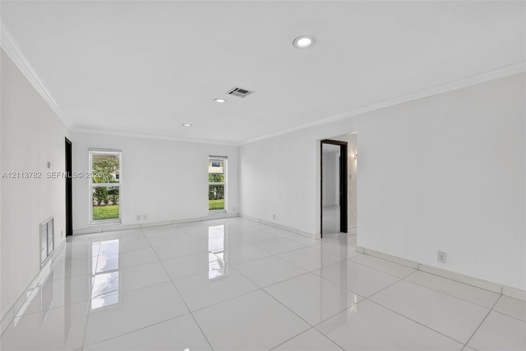 Bright living area featuring large-format polished tile flooring, recessed lighting, crown molding, and dual windows