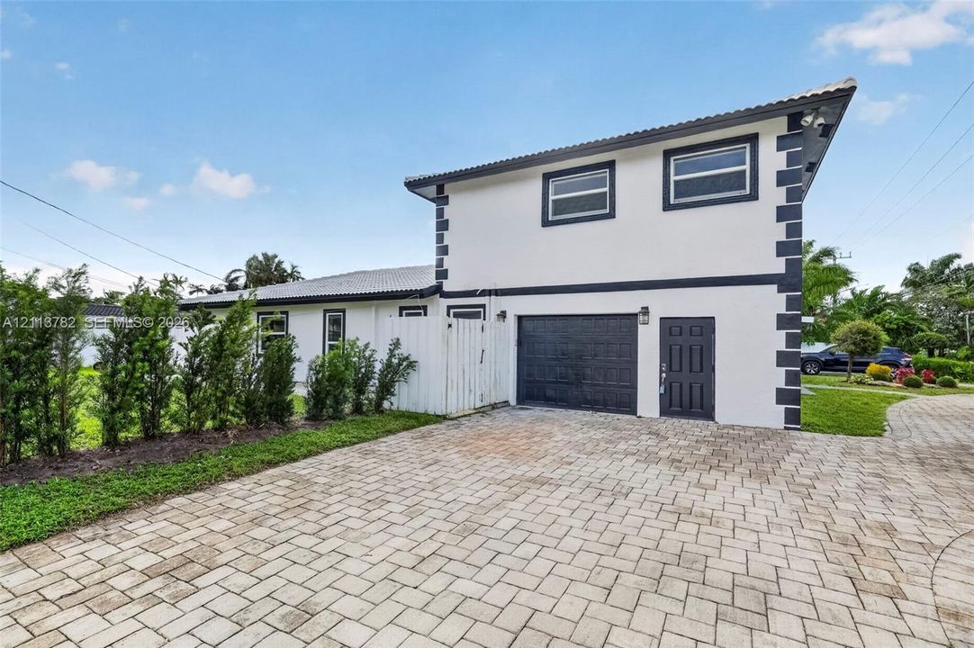 Two-story exterior featuring a high-contrast facade, paver driveway, single-car garage, and perimeter landscaping