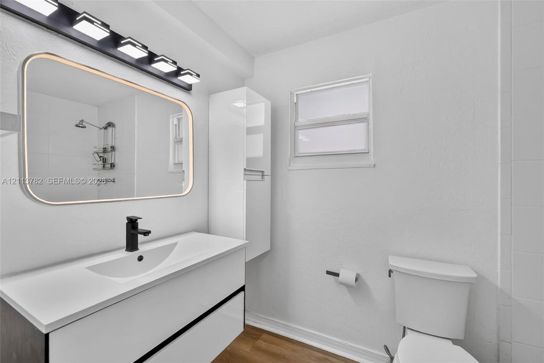 Bathroom featuring a floating vanity with a integrated basin, matte black faucet, wall-mounted storage cabinet, and large rectangular mirror with perimeter lighting