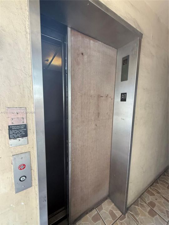 Entryway featuring two brown multi-panel doors with metallic hardware and a recessed fire extinguisher cabinet