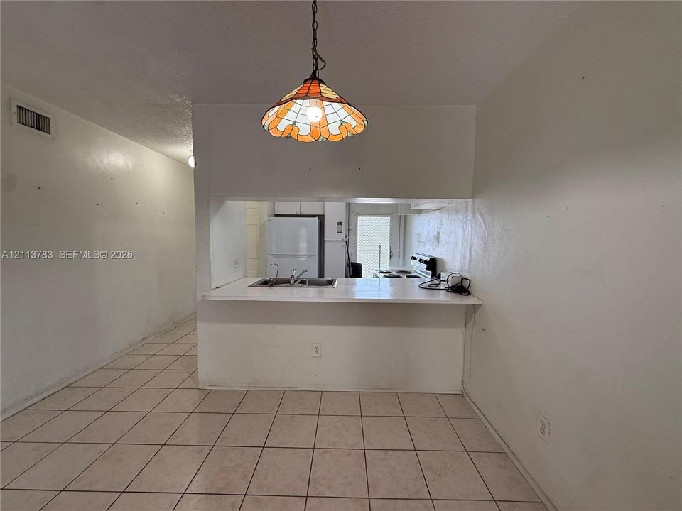 Pass-through kitchen counter with an integrated dual-basin stainless steel sink, tile flooring, and a decorative stained-glass pendant light fixture
