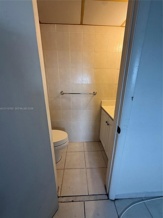 Bathroom featuring floor-to-ceiling tiled walls, a built-in vanity with a molded sink basin, tiled flooring, a bathtub-shower combination with a wall-mounted spray fixture, and a single-pane window