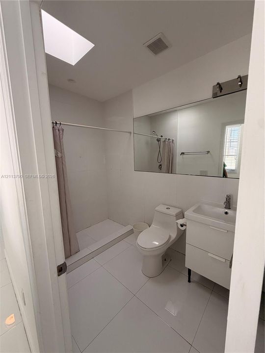 Bathroom featuring a skylight, full-width wall mirror, white tiled flooring, walk-in shower, and a white two-drawer vanity