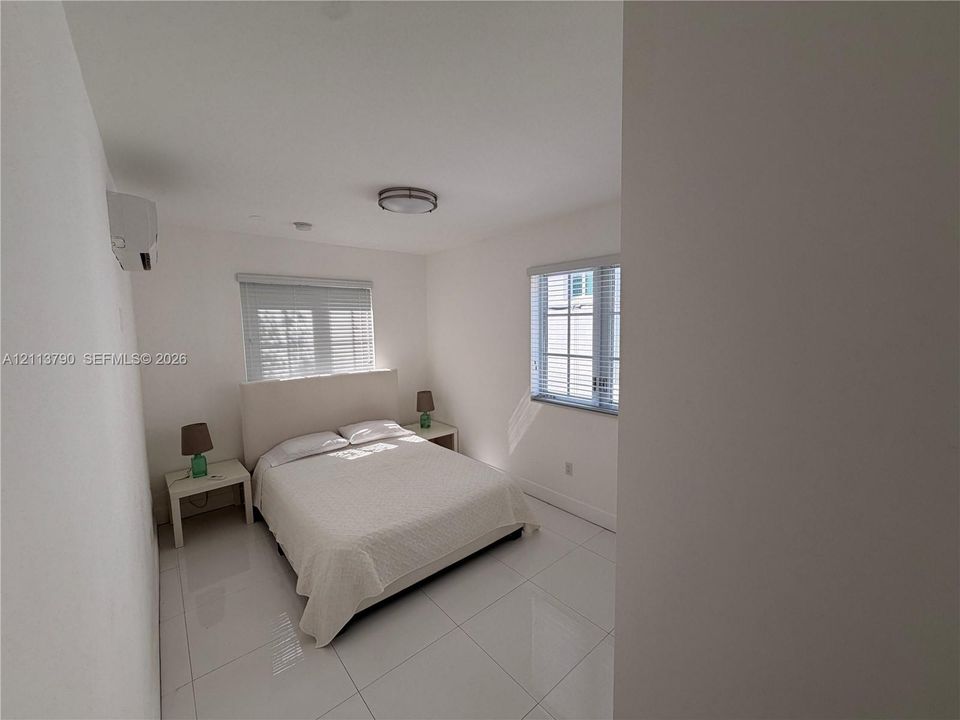 Neutral-toned room featuring large-format tile flooring, dual windows with blinds, and a wall-mounted ductless heating and cooling unit