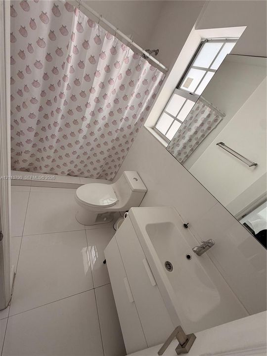 Bathroom featuring large-format ceramic tile flooring, a wall-mounted vanity with a rectangular integrated sink, a full-width mirror, and a combined tub and shower enclosure with a single-handle faucet