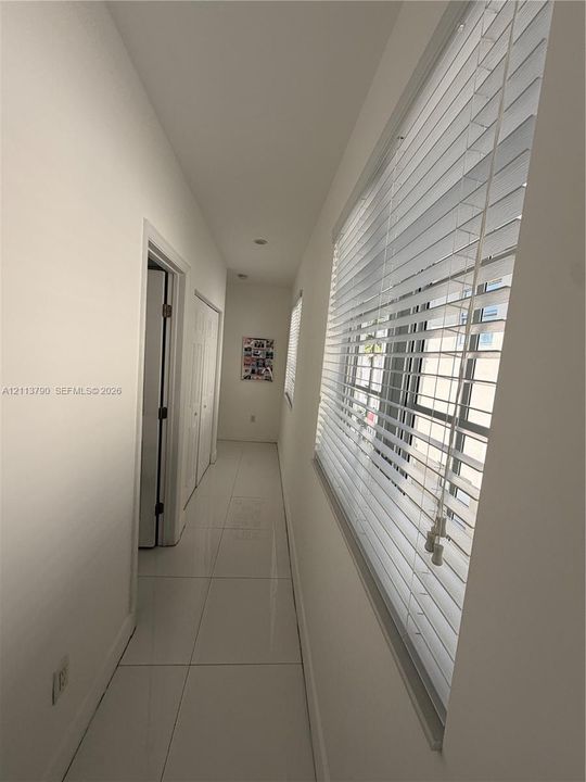 Hallway featuring large-format tile flooring, recessed ceiling lighting, and windows equipped with horizontal blinds