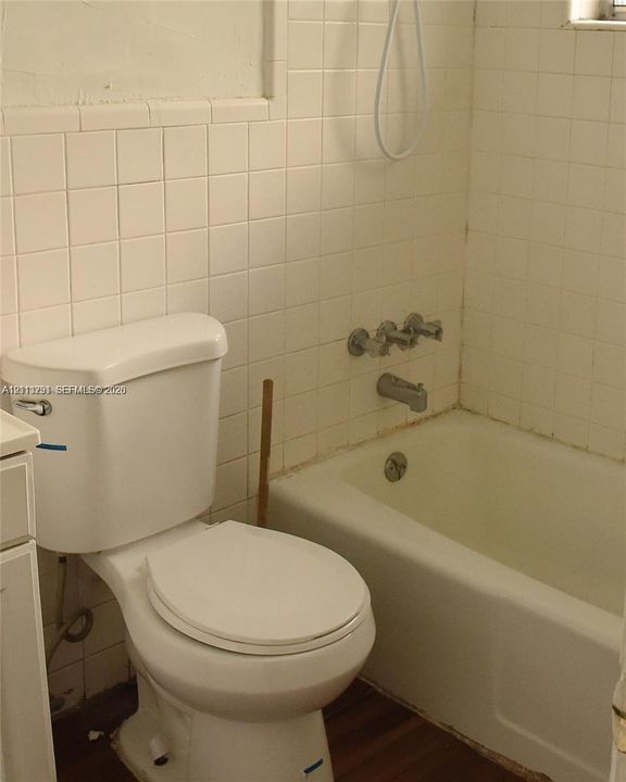 Bathroom featuring a white porcelain toilet, integrated bathtub and shower combination, and wall-mounted metallic fixtures