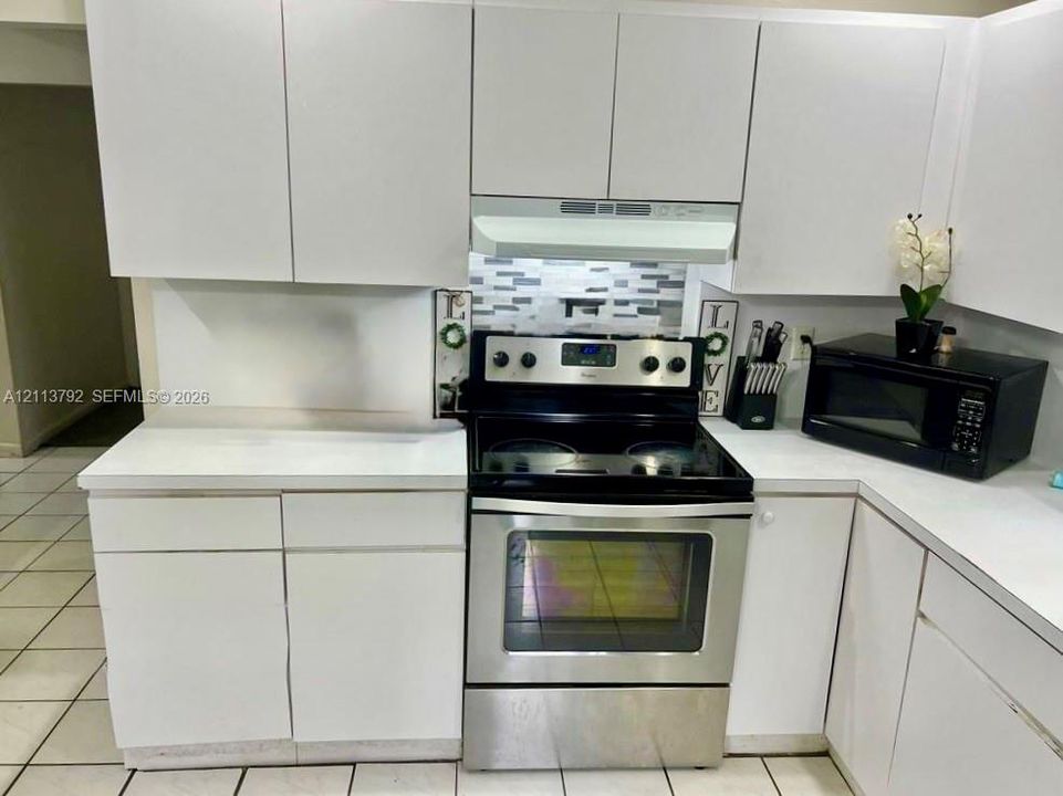 Kitchen featuring white cabinetry, stainless steel range, matching over-the-range hood, mosaic tile backsplash, and light-toned floor tile