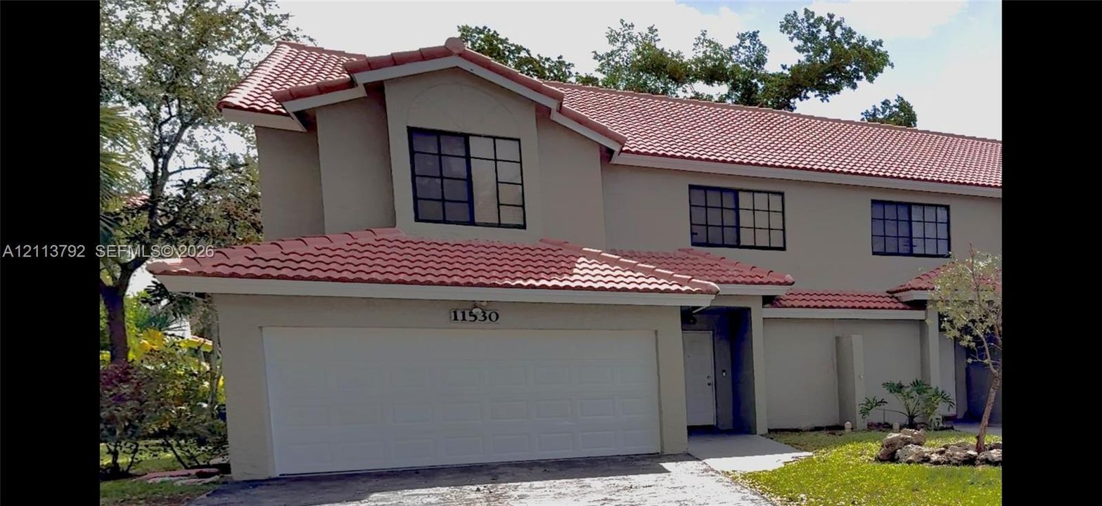 Two-story exterior featuring a terracotta-tiled roof, light-toned stucco facade, multi-pane windows, and an attached two-car garage
