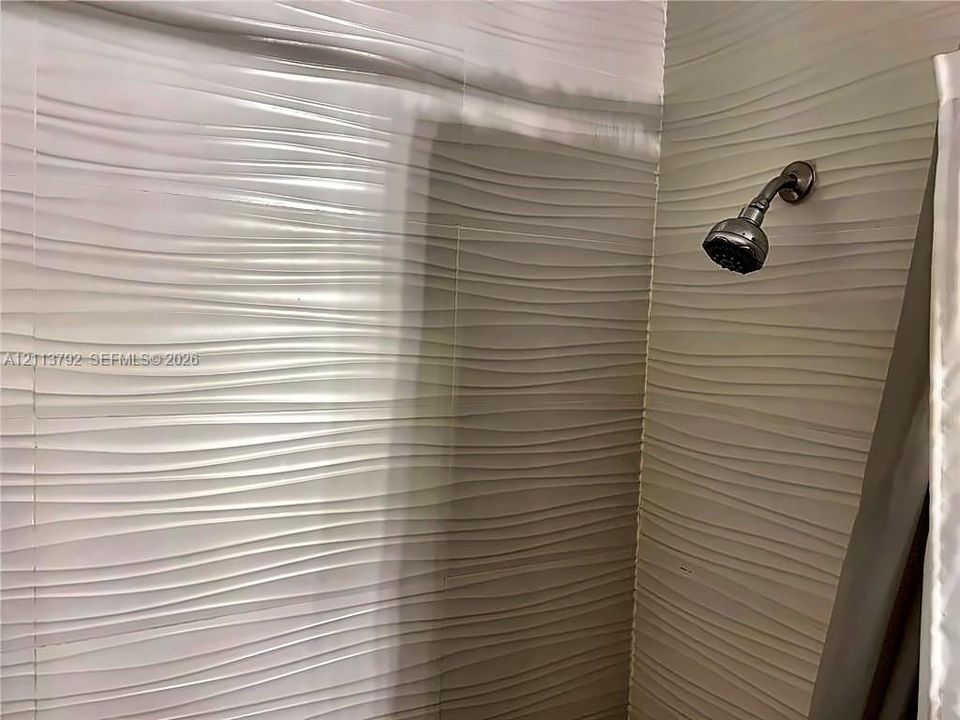 Textured wall tiles featuring a horizontal wave pattern and a wall-mounted shower head with a metallic finish