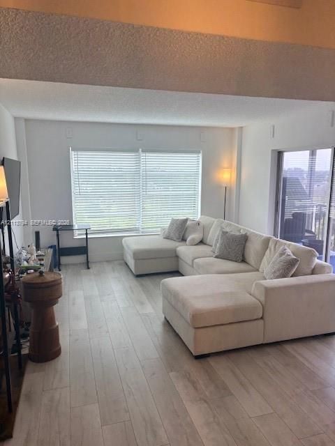 Open living area featuring wood-finish flooring, vaulted ceilings, large windows with horizontal blinds, and a sliding glass door
