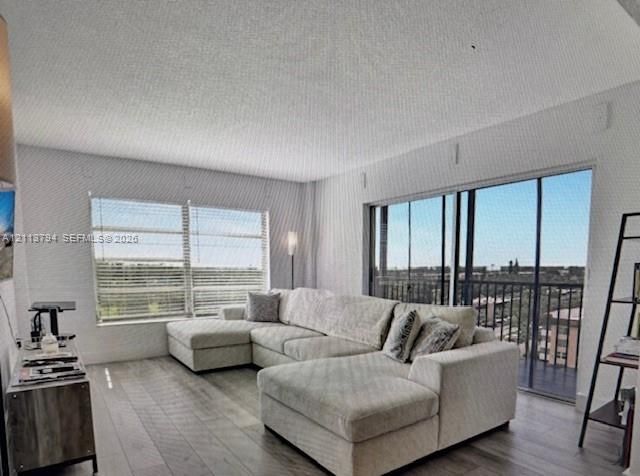 Living area featuring wood-finish flooring, expansive floor-to-ceiling sliding glass doors with balcony access, and oversized windows