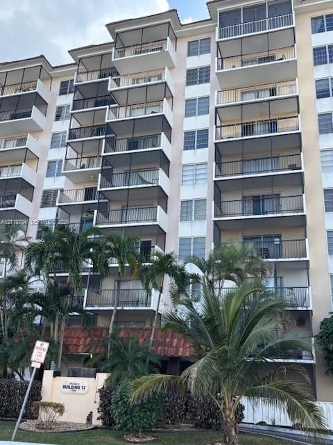 Multi-story building exterior featuring screened balconies, horizontal sliding windows, tile roofing accents, and tropical landscaping
