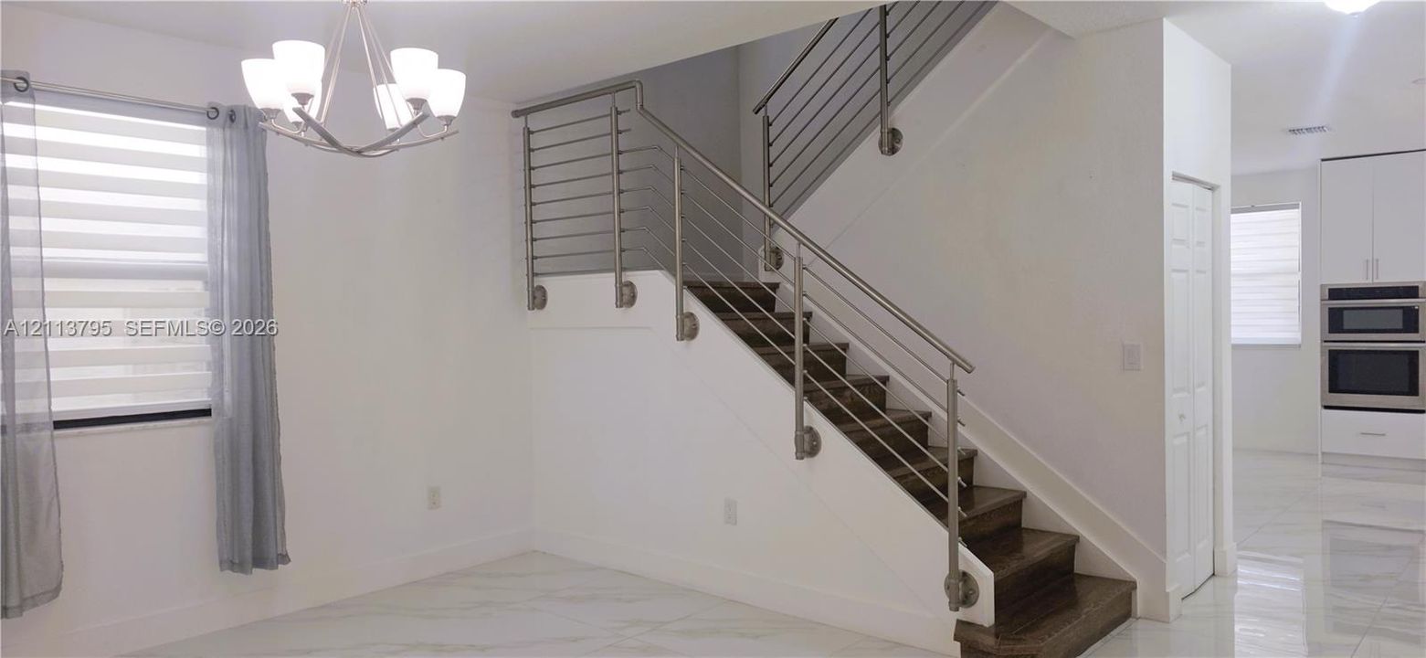 Staircase featuring dark wood-finish treads and a modern horizontal cable railing system, polished stone-finish flooring, and a multi-light chandelier
