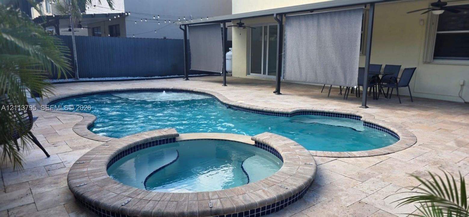 Outdoor patio featuring natural stone pavers, a swimming pool with a built-in spa, a covered terrace with ceiling fans, and retractable privacy screens