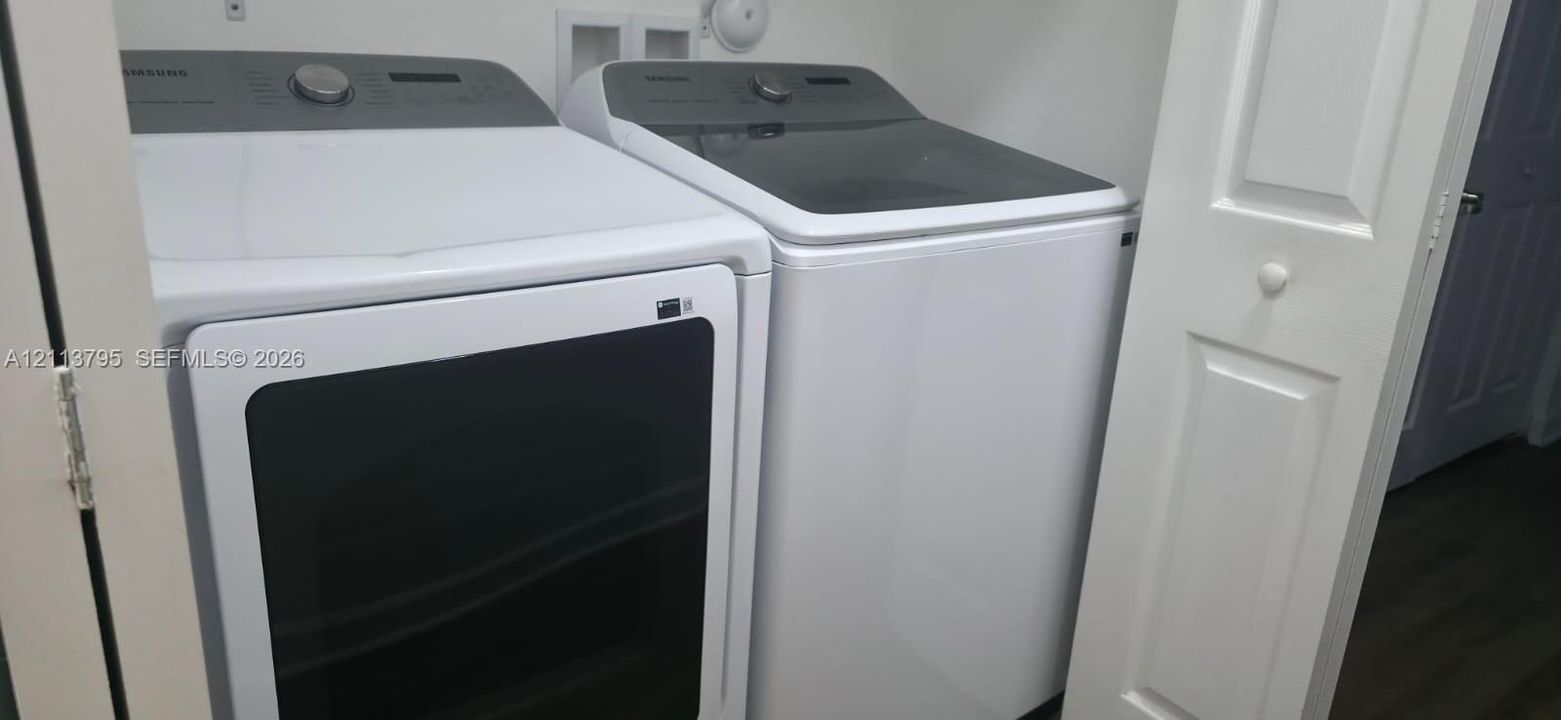 Laundry area featuring white top-load washer and front-load dryer with glass door panels, housed within a closet featuring paneled bi-fold doors