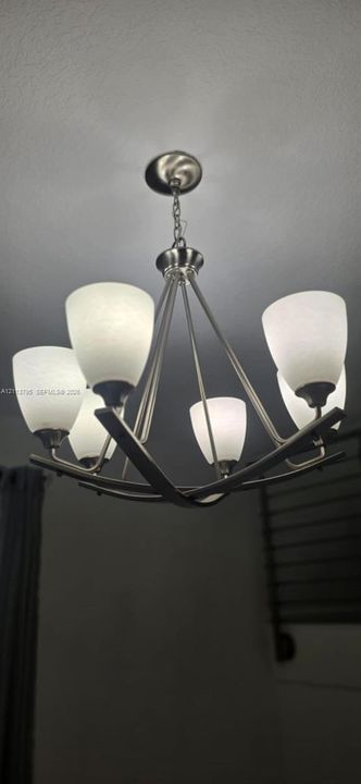 Five-light chandelier featuring a brushed metal finish, curved structural arms, and frosted glass shades