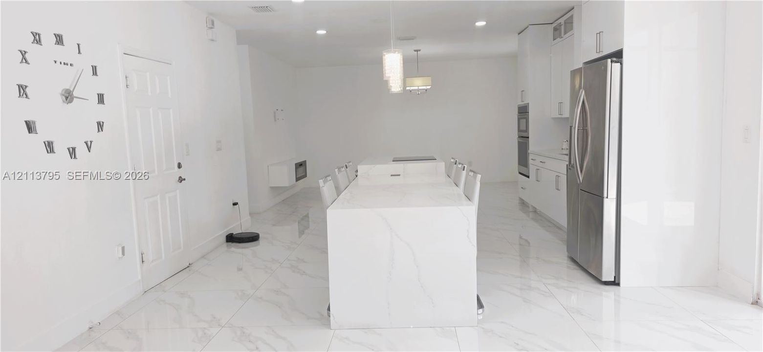Kitchen featuring a large central island with solid-surface countertop, white cabinetry, stainless steel appliances including a built-in double oven, and large-format porcelain tile flooring