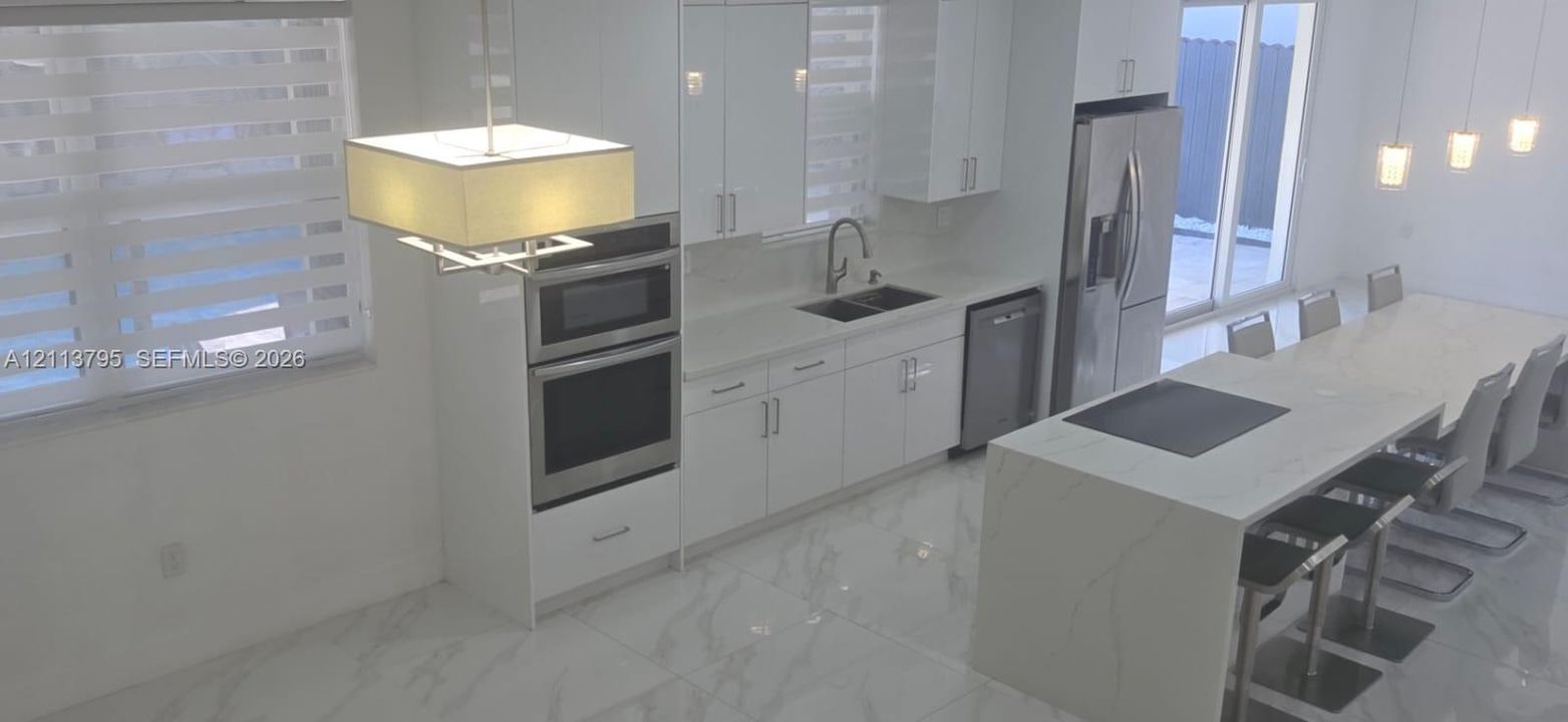 Kitchen featuring white cabinetry, stone-finish countertops, stainless steel wall ovens, a center island with integrated seating, and large-format tile flooring