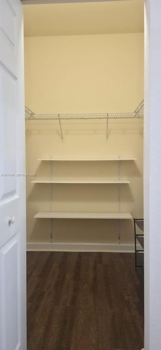 Storage space featuring wood-finish flooring, adjustable white shelving, and a metal wire rack