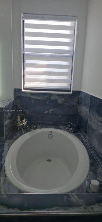 Oval soaking tub featuring large-format dark stone-patterned wall tiling and a built-in deck surround