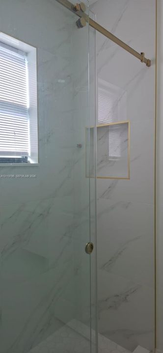 Shower enclosure featuring floor-to-ceiling veined tile, frameless glass sliding door with metallic hardware, recessed wall niche, and hexagonal floor tile