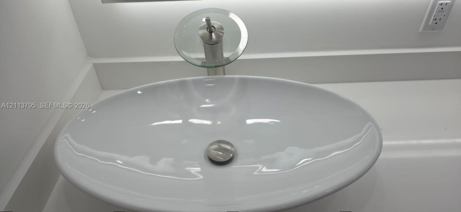 Oval vessel sink featuring a brushed metal waterfall faucet with a glass disk spout, set into a solid-surface countertop with an integrated backsplash