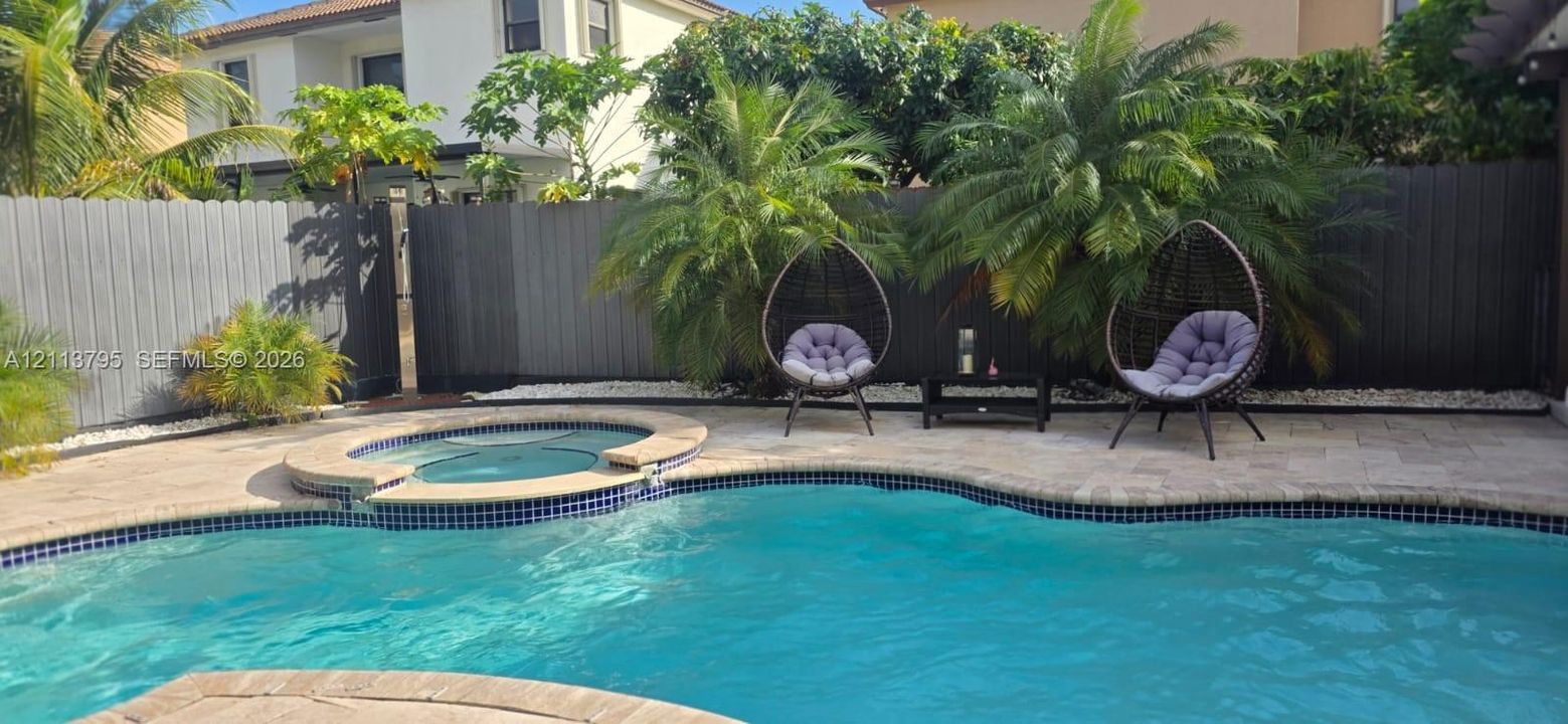 Swimming pool with built-in spa, stone-finish paver decking, and solid-panel privacy fencing
