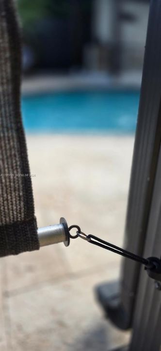 Retractable privacy screen featuring a textured mesh panel, metal anchor hardware, and stone-finish patio surfacing with an in-ground pool