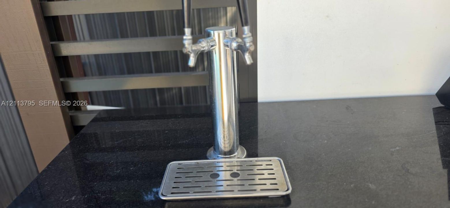 Built-in dual-tap chrome beverage dispenser with a stainless steel drip tray, set into a stone countertop
